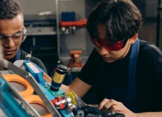 Two young engineers concentrating on precision work in a technical workshop, wearing safety goggles.