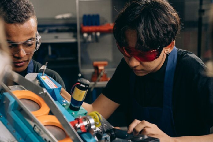 Two young engineers concentrating on precision work in a technical workshop, wearing safety goggles. Two young engineers concentrating on precision work in a technical workshop, wearing safety goggles.