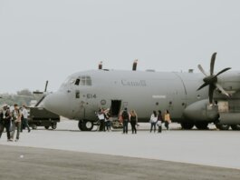 A Canadian military transport aircraft on a runway with people boarding.