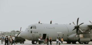 A Canadian military transport aircraft on a runway with people boarding.