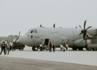 A Canadian military transport aircraft on a runway with people boarding.