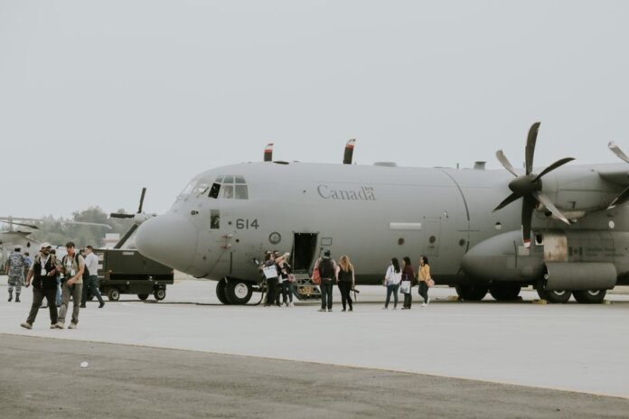 A Canadian military transport aircraft on a runway with people boarding.