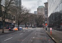 A city street with tents showing urban homelessness beneath bare trees on cloudy day.