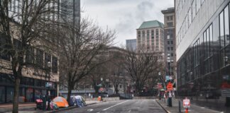 A city street with tents showing urban homelessness beneath bare trees on cloudy day.