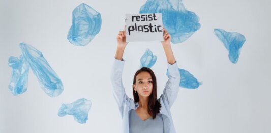 A determined woman holds a sign against plastic pollution amidst floating bags.
