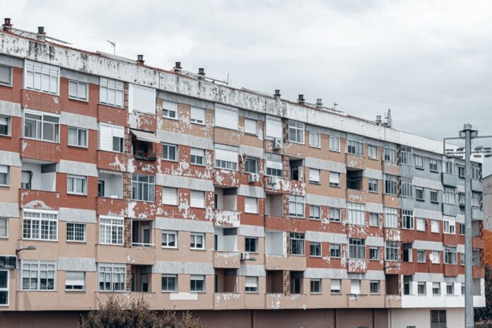 A large urban apartment block featuring a weathered facade with peeling paint and balconies. A large urban apartment block featuring a weathered facade with peeling paint and balconies.