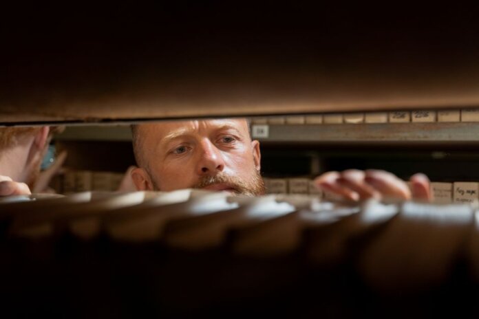 A man searches through archives in an office storage room, focused and working.