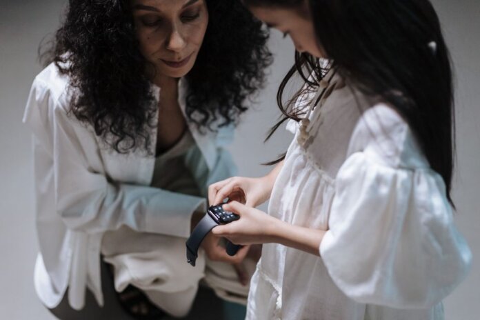 A mother and daughter interact with a smartwatch, showcasing family bonding with modern tech. A mother and daughter interact with a smartwatch, showcasing family bonding with modern tech.