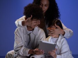 A mother covering her children's eyes while they hold a tablet, illustrating parental control.