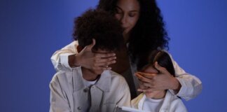 A mother covering her children's eyes while they hold a tablet, illustrating parental control.