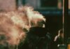 Сезон дыма возвращается: лесные пожары меняют канадское лето A person in a hoodie exhaling smoke in an abstract and ethereal urban environment.