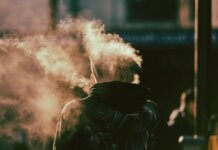 Сезон дыма возвращается: лесные пожары меняют канадское лето A person in a hoodie exhaling smoke in an abstract and ethereal urban environment.