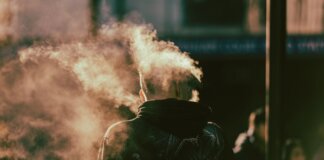 A person in a hoodie exhaling smoke in an abstract and ethereal urban environment.