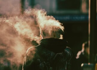 Сезон дыма возвращается: лесные пожары меняют канадское лето A person in a hoodie exhaling smoke in an abstract and ethereal urban environment.