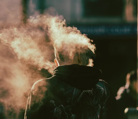A person in a hoodie exhaling smoke in an abstract and ethereal urban environment.