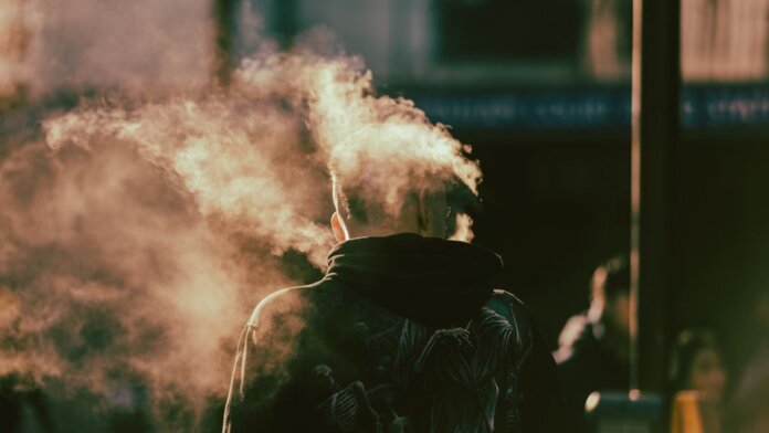 A person in a hoodie exhaling smoke in an abstract and ethereal urban environment. A person in a hoodie exhaling smoke in an abstract and ethereal urban environment.