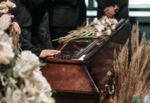 24-летняя женщина погибла в ДТП на шоссе в Гамильтоне A poignant funeral moment with mourners gathered around a coffin decorated with flowers.