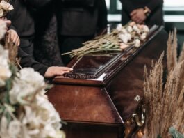 A poignant funeral moment with mourners gathered around a coffin decorated with flowers.
