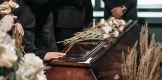 A poignant funeral moment with mourners gathered around a coffin decorated with flowers.