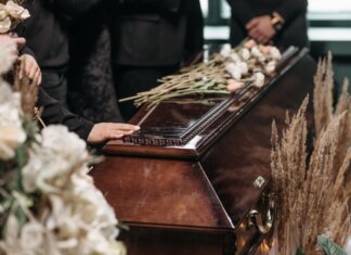 A poignant funeral moment with mourners gathered around a coffin decorated with flowers.
