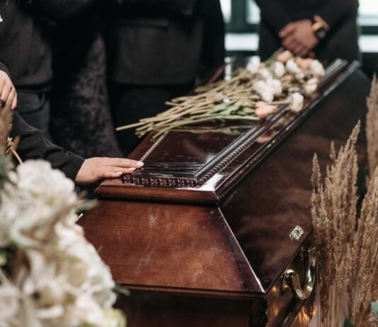 A poignant funeral moment with mourners gathered around a coffin decorated with flowers.