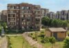 A scenic view of a modern apartment complex surrounded by greenery under a clear blue sky.