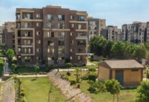 A scenic view of a modern apartment complex surrounded by greenery under a clear blue sky.