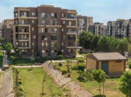 A scenic view of a modern apartment complex surrounded by greenery under a clear blue sky.