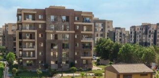 A scenic view of a modern apartment complex surrounded by greenery under a clear blue sky.
