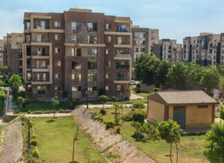 A scenic view of a modern apartment complex surrounded by greenery under a clear blue sky.