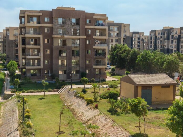 A scenic view of a modern apartment complex surrounded by greenery under a clear blue sky. A scenic view of a modern apartment complex surrounded by greenery under a clear blue sky.