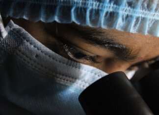 A scientist in protective gear intensely looking through a microscope.