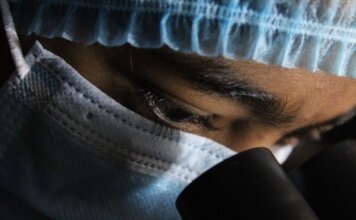 Учёные открыли скрытую систему очистки человеческого глаза A scientist in protective gear intensely looking through a microscope.