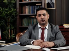 A serious businessman in a suit writing at his desk in a formal office setting.