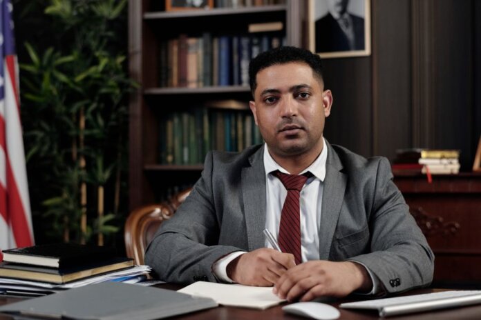 A serious businessman in a suit writing at his desk in a formal office setting. A serious businessman in a suit writing at his desk in a formal office setting.