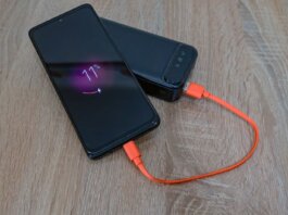 A smartphone charging from a power bank with an orange cable on a wooden table.