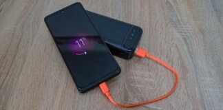 A smartphone charging from a power bank with an orange cable on a wooden table.