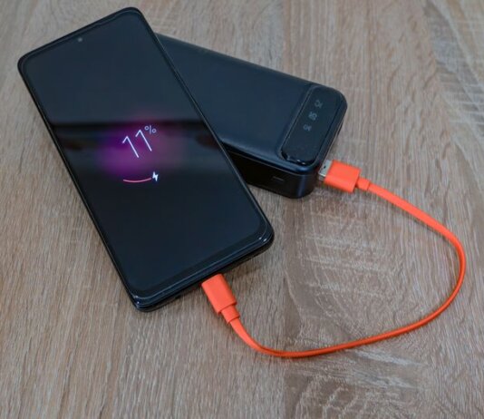 A smartphone charging from a power bank with an orange cable on a wooden table.