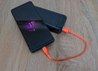 A smartphone charging from a power bank with an orange cable on a wooden table.