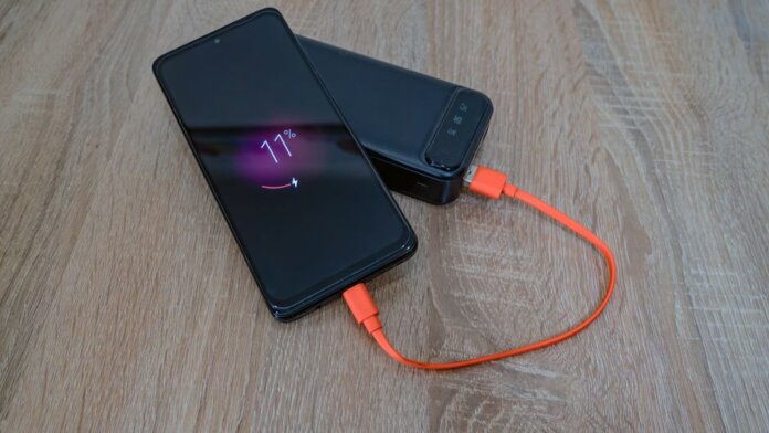 A smartphone charging from a power bank with an orange cable on a wooden table. A smartphone charging from a power bank with an orange cable on a wooden table.