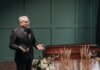 Ньюфаундленд выделил более $531 тыс. на пожарное оборудование A solemn funeral ceremony featuring a pastor in a black suit delivering a speech next to a wooden coffin adorned with flowers.