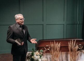 Ньюфаундленд выделил более $531 тыс. на пожарное оборудование A solemn funeral ceremony featuring a pastor in a black suit delivering a speech next to a wooden coffin adorned with flowers.