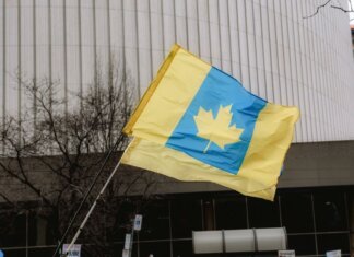 Канада станет со-рамочной нацией многонациональной дивизии НАТО в Латвии A unique flag blending Ukrainian colors with a Canadian maple leaf in an outdoor setting.