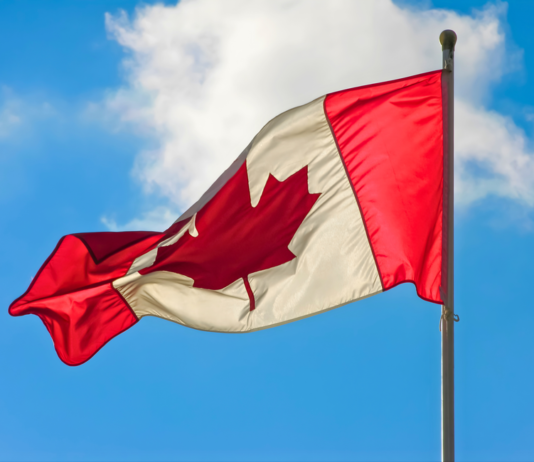 A vibrant Canadian flag waving against a blue sky with clouds.