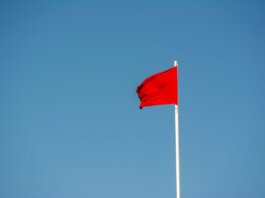 A vibrant red flag waving on a tall pole against a clear, blue sky.