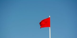 A vibrant red flag waving on a tall pole against a clear, blue sky.
