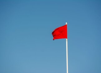 A vibrant red flag waving on a tall pole against a clear, blue sky.