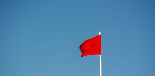 A vibrant red flag waving on a tall pole against a clear, blue sky.