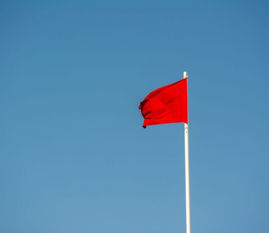 A vibrant red flag waving on a tall pole against a clear, blue sky.