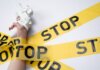 A white toy gun held by a hand wrapped in yellow stop tape on a white background, conveying a message of caution.